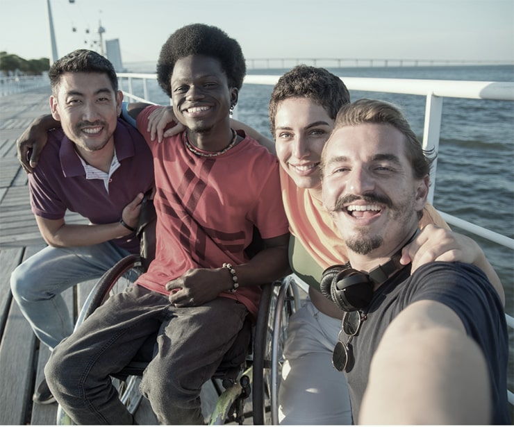 Four people are sitting on a dock with water behind them. They are looking at the camera and smiling.